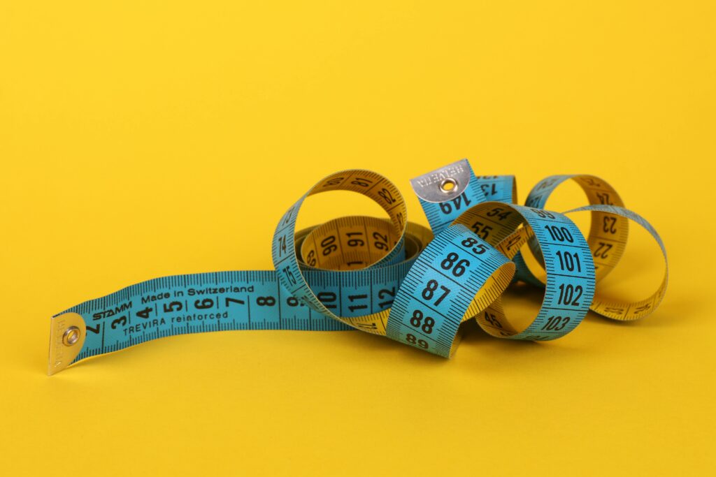 Colorful measuring tape curled up on a vibrant yellow background, ideal for design concepts.