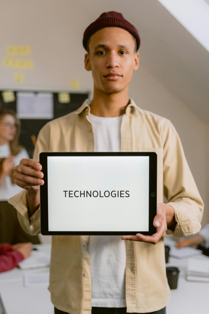 A young man holding a tablet displaying the word 'Technologies' in an indoor office setting.