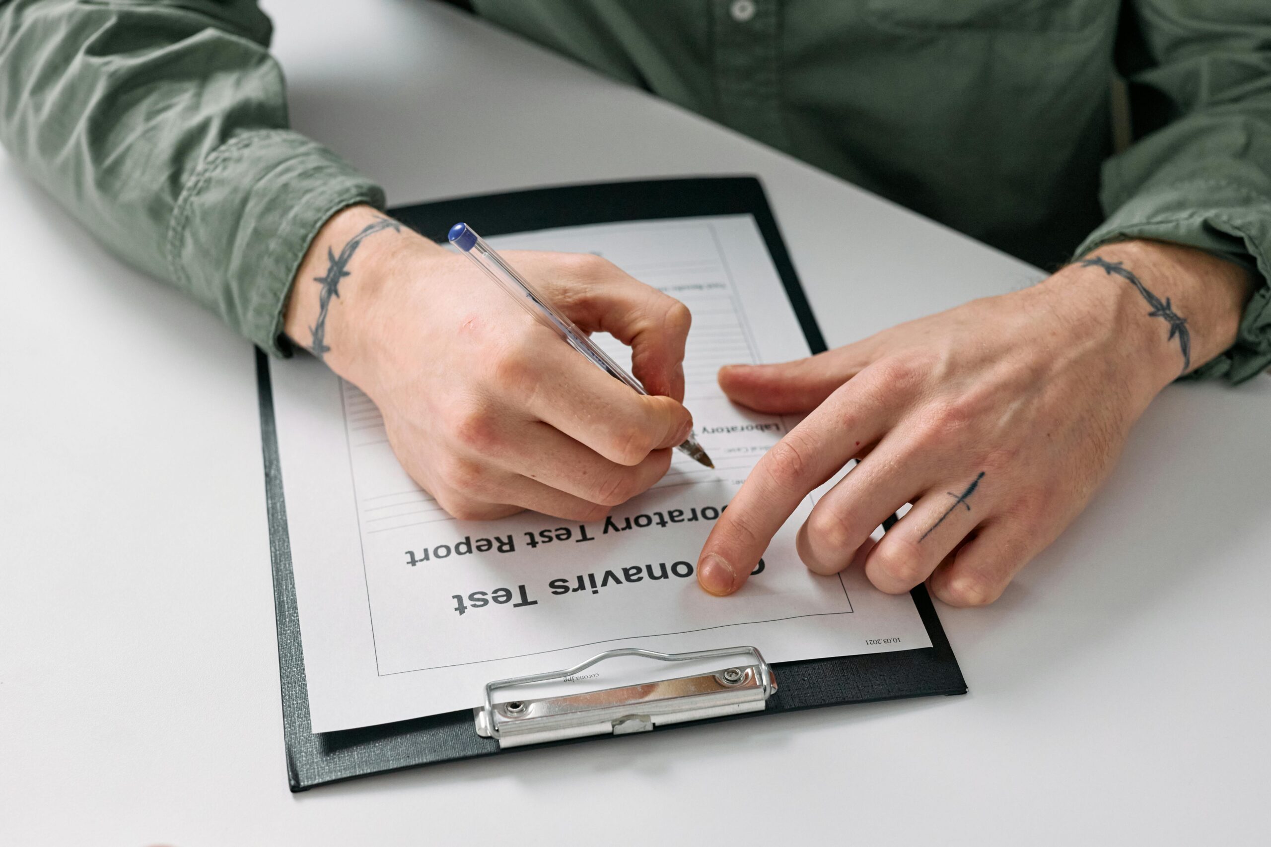 A person with tattoos writes on an honesty test report using a pen and notepad.