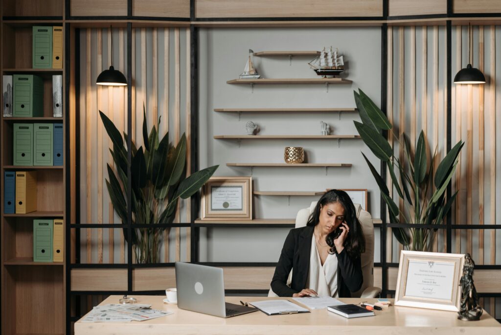 Businesswoman at desk in a stylish office, engaged in phone conversation with paperwork.