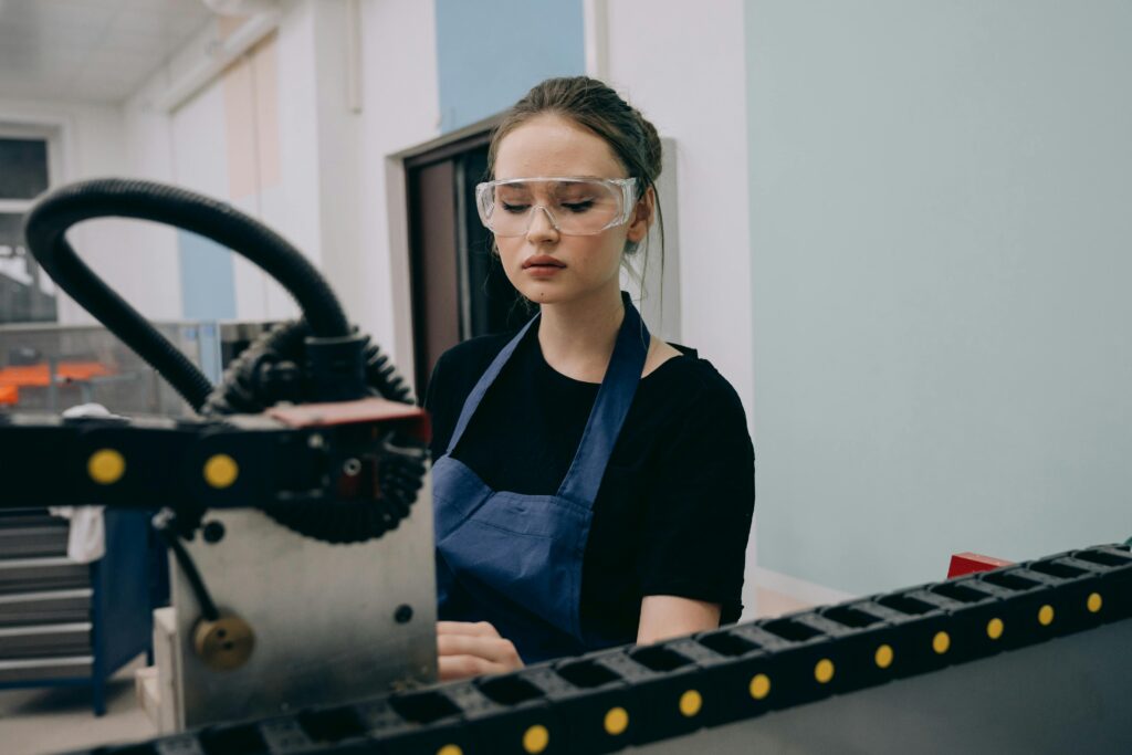 A female engineer operates machinery with precision in an industrial setting, wearing safety glasses.