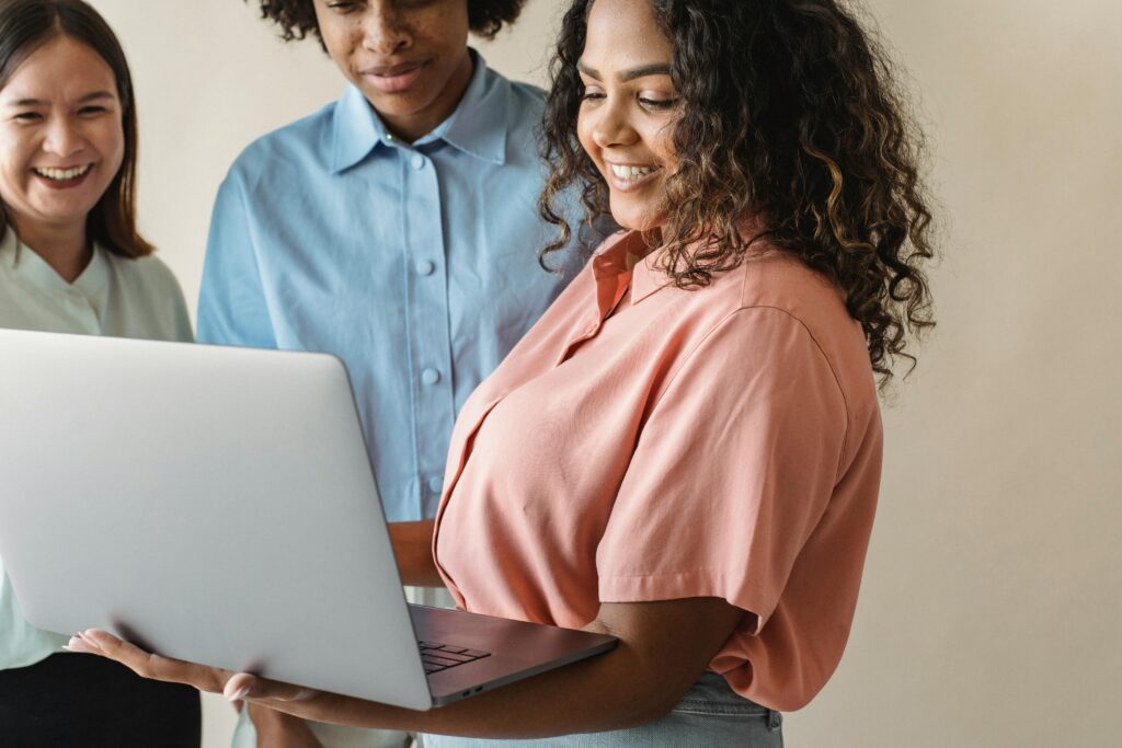Three diverse women collaborating and enjoying work on a laptop with smiles.
